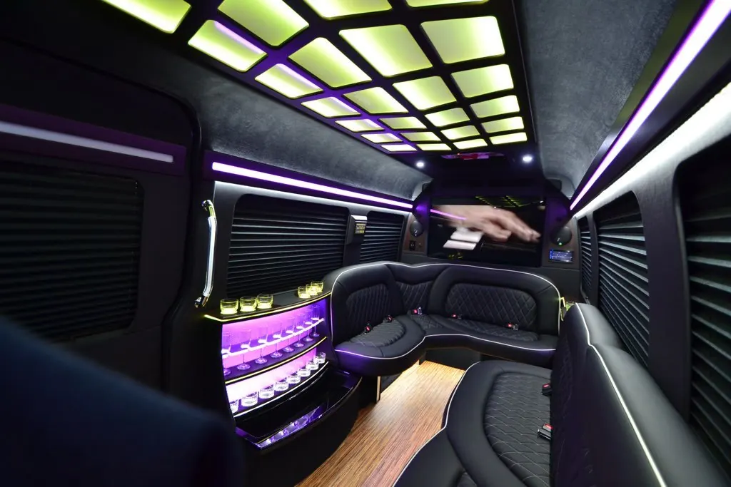 Mercedes Sprinter limo interior with leather bench seating, LED ceiling and a lit glass bar